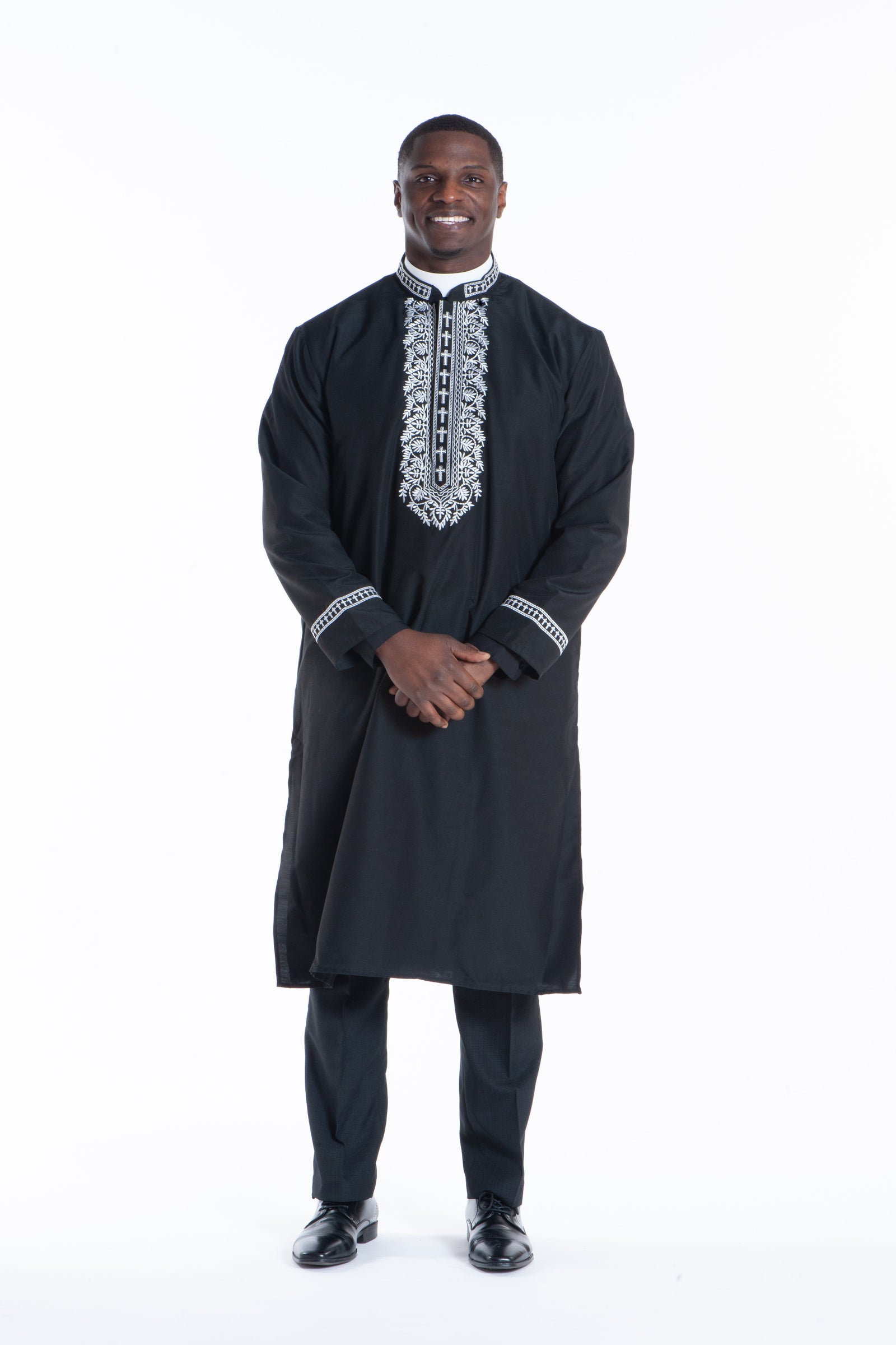 Clergy Kurtas for Men: A black kurta with intricate embroidery, worn by a smiling man standing confidently.