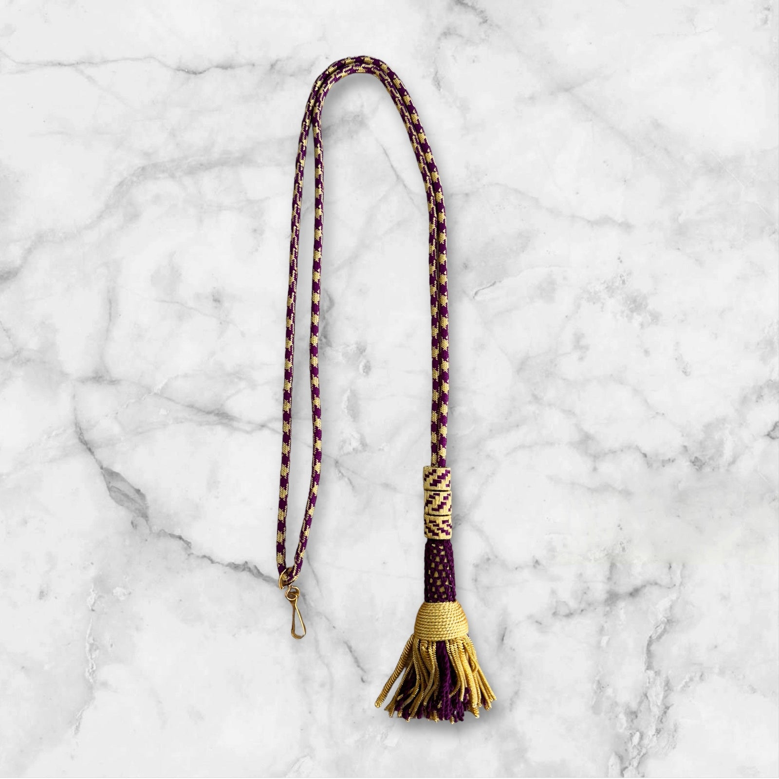 Ceremonial and Graduation Cords in purple and gold colors displayed on a marble background.