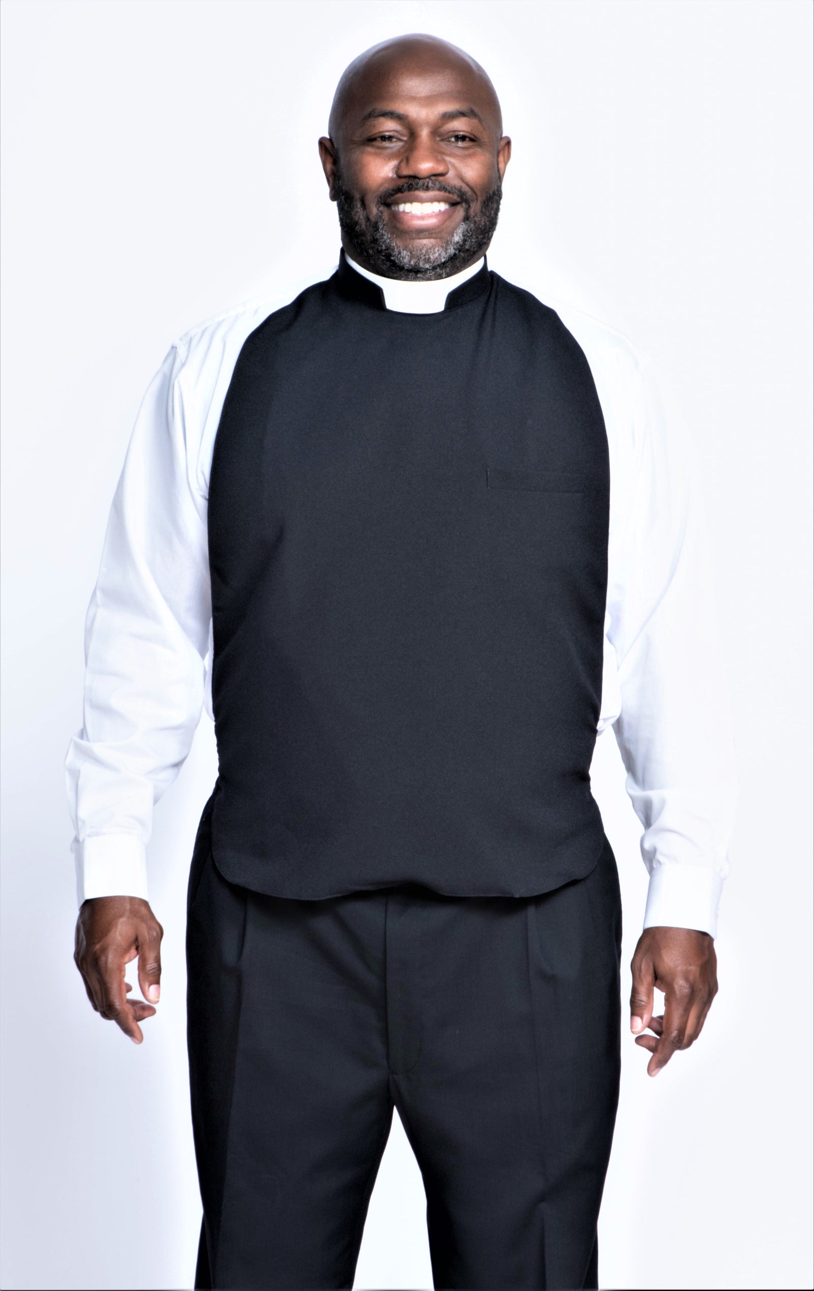 Smiling man wearing a black clergy rabat over a white shirt, representing traditional clergy attire.