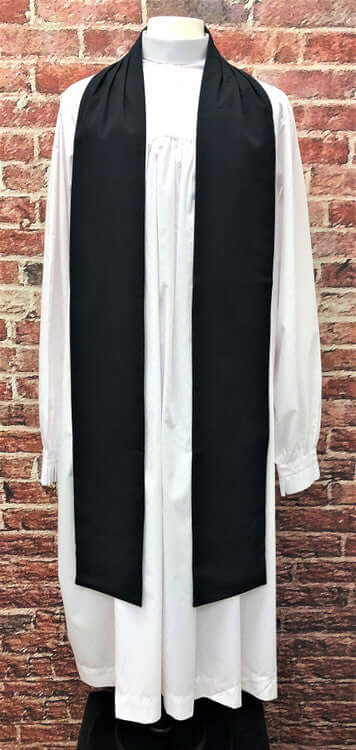 Tippet In Black displayed on a mannequin alongside a white clergy robe against a brick background.